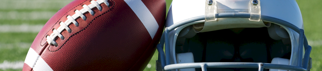 A brown American football and blue helmet rest on green grass, like for game day practice or kickoff.