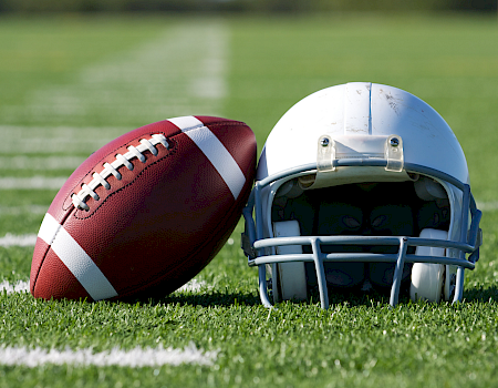 A brown American football and blue helmet rest on green grass, like for game day practice or kickoff.