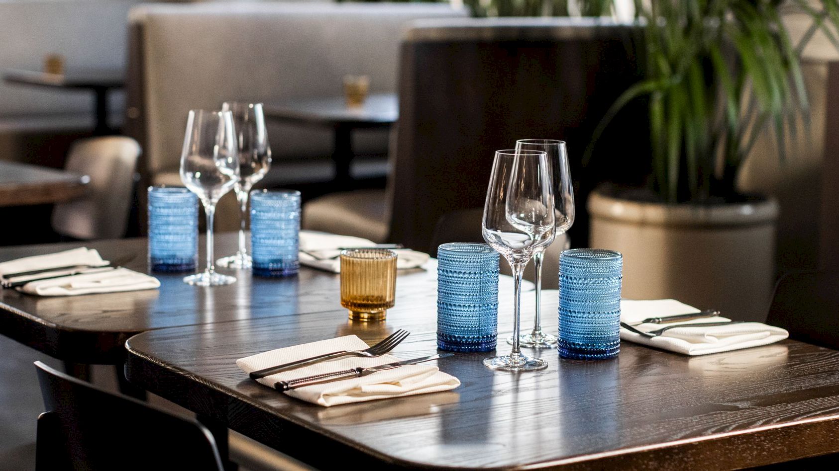 A set restaurant table with wine glasses, cutlery, napkins, and blue and gold candle holders, ready for dining.