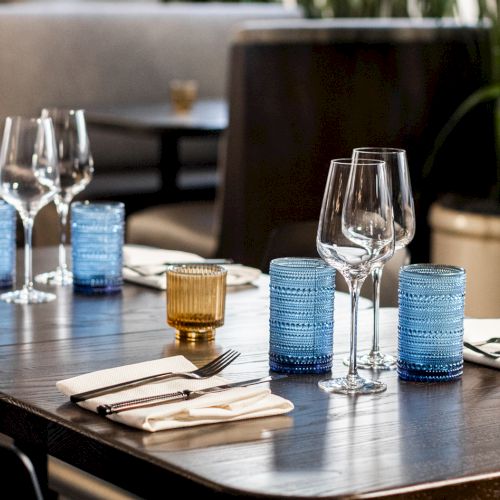 A set dining table with wine glasses, neatly folded napkins, silverware, and blue candle holders in a restaurant setting.
