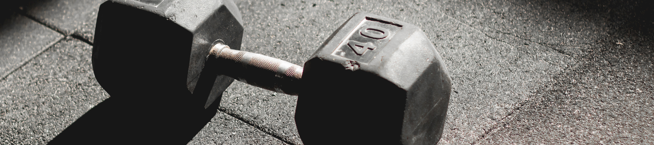 A pair of black rubber dumbbells with 10 marked on each weight, resting on a concrete floor.