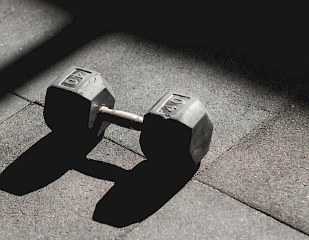 A pair of black rubber dumbbells with 10 marked on each weight, resting on a concrete floor.